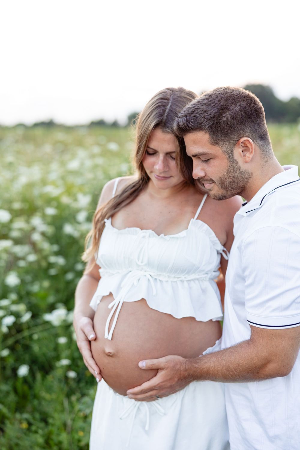 Expecting couple embracing in flower field, man tenderly holding pregnant belly.