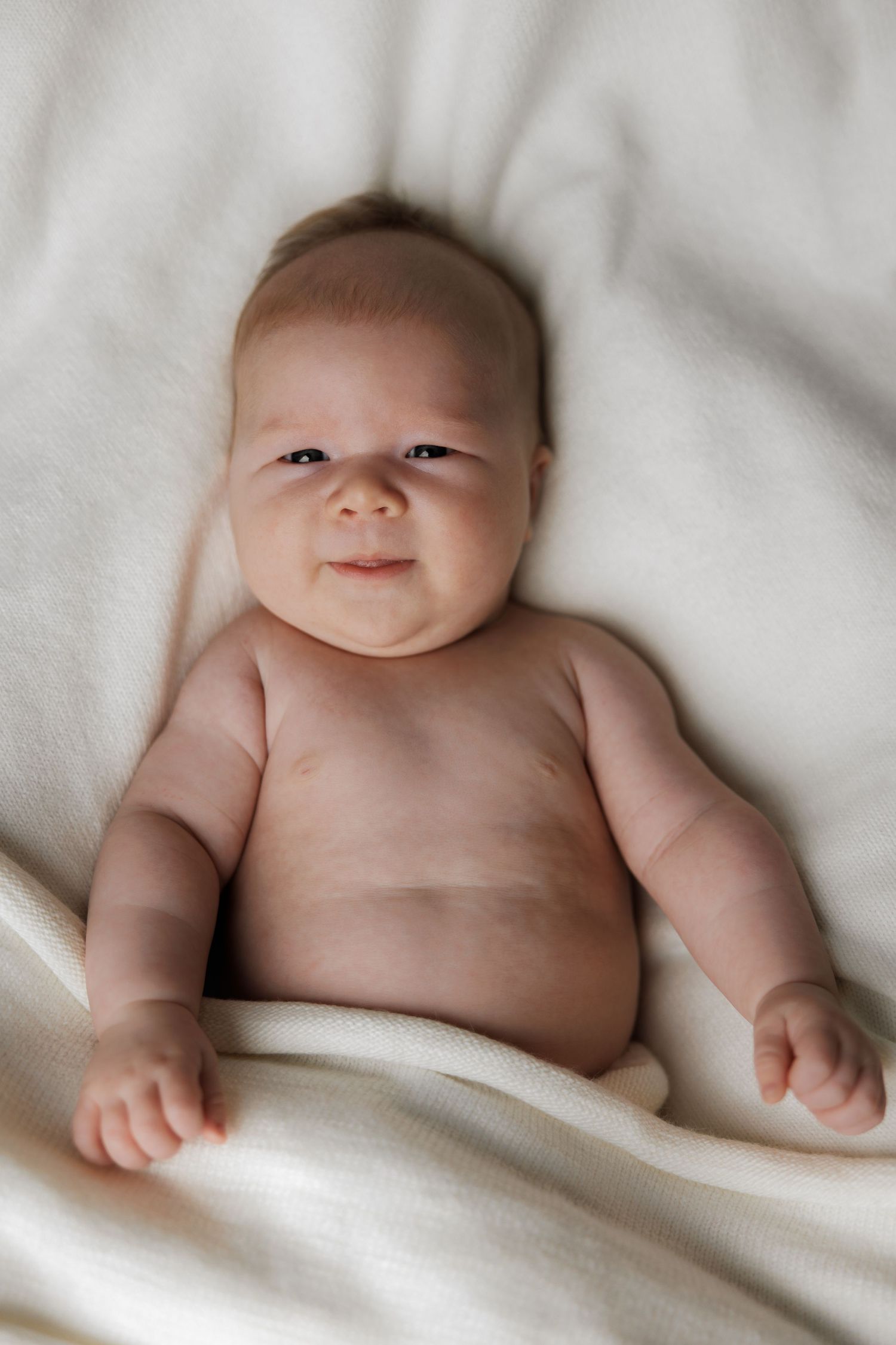 Adorable newborn baby lying on a soft white blanket, smiling with chubby cheeks and bright eyes.