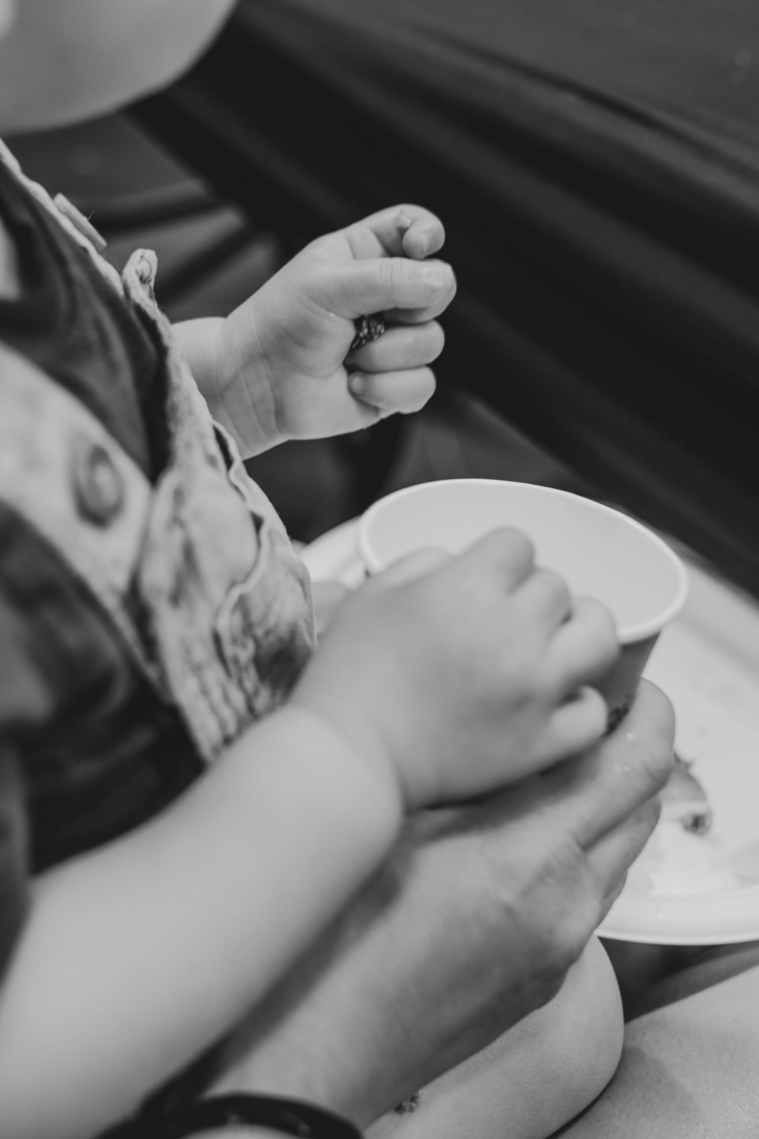 Black and white photo of hands holding a white cup and saucer, with a spoon being stirred.