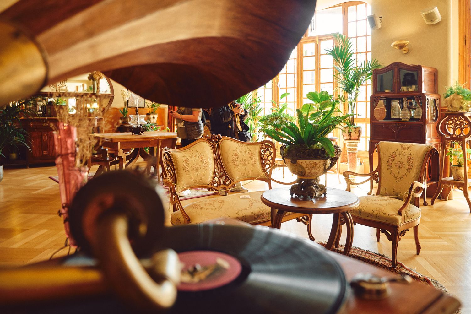 Vintage gramophone with vinyl record in elegant antique living room with ornate furniture and tropical plants.