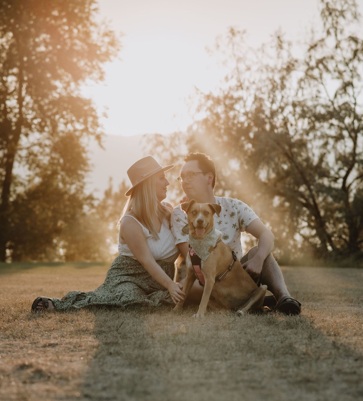 Bride and groom hold hands in golden field with mountain lake backdrop during outdoor wedding photo session.