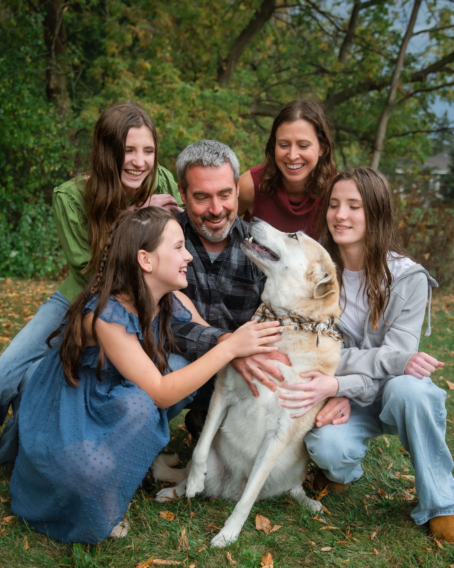 Family of four with German Shepherd dog posing outdoors among autumn foliage for a fall portrait photo.
