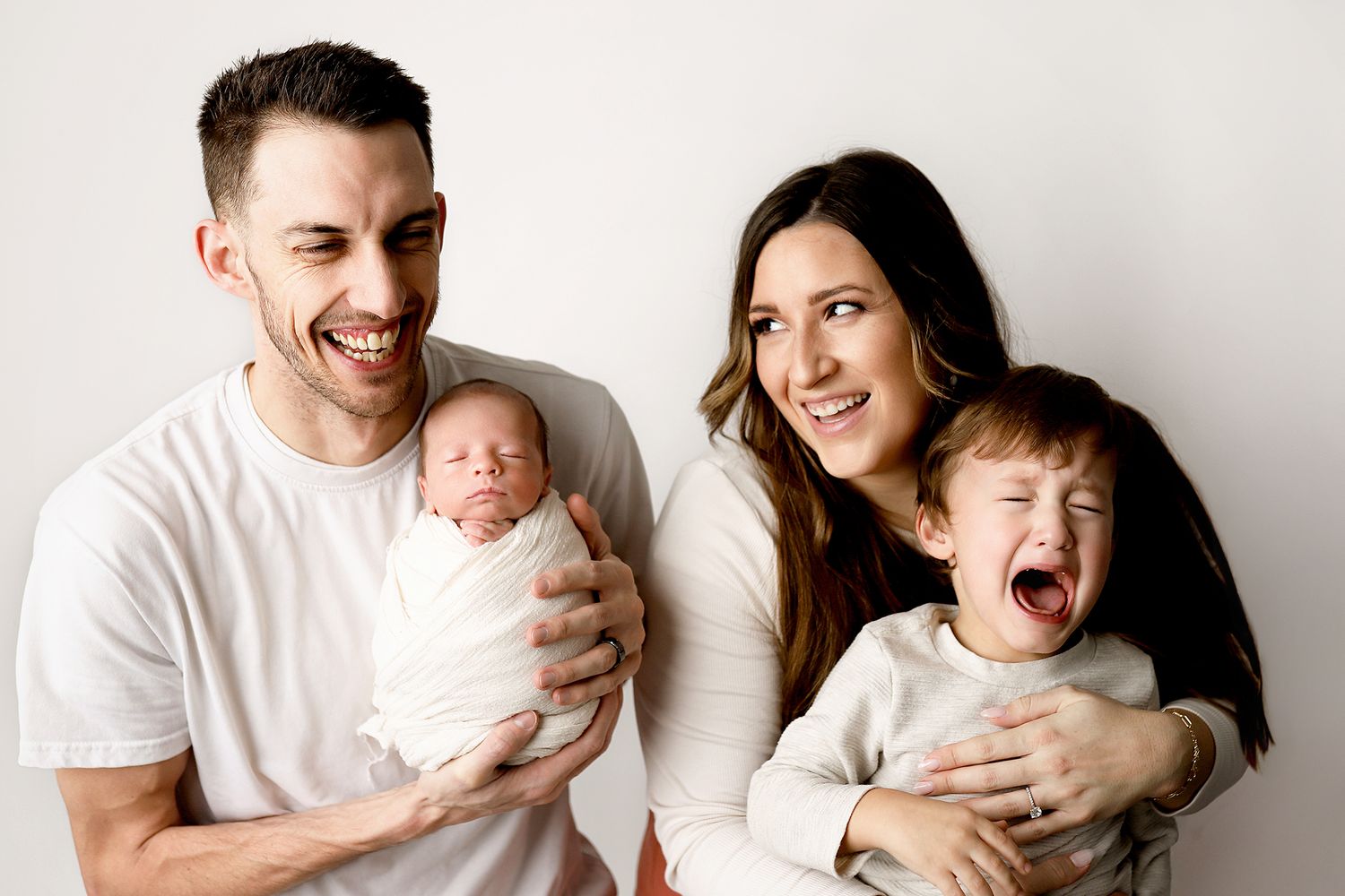 Happy family with parents holding newborn baby and toddler posing for portrait photo on white background.