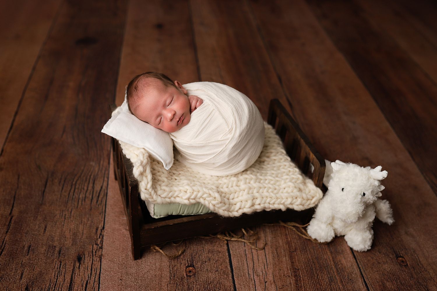 Newborn baby swaddled in white wrap sleeping peacefully in a wooden crib with a white teddy bear beside them. Utah newborn photographer