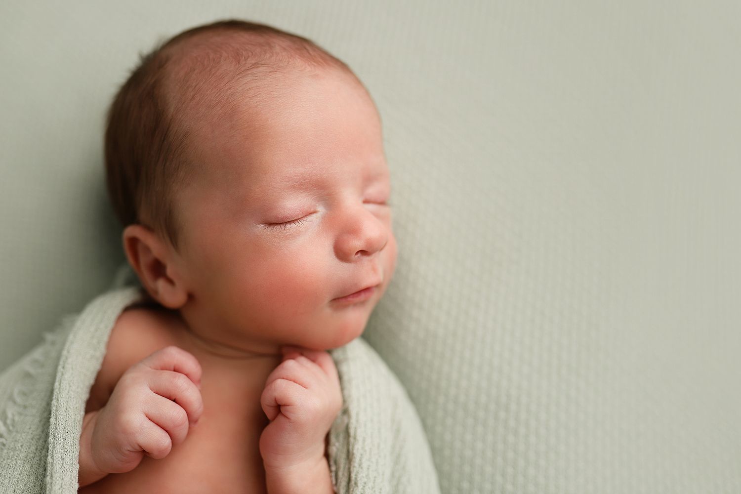 Peaceful newborn baby sleeping wrapped in a soft green blanket on a mint background. Orem newborn photographer. Utah County photographer