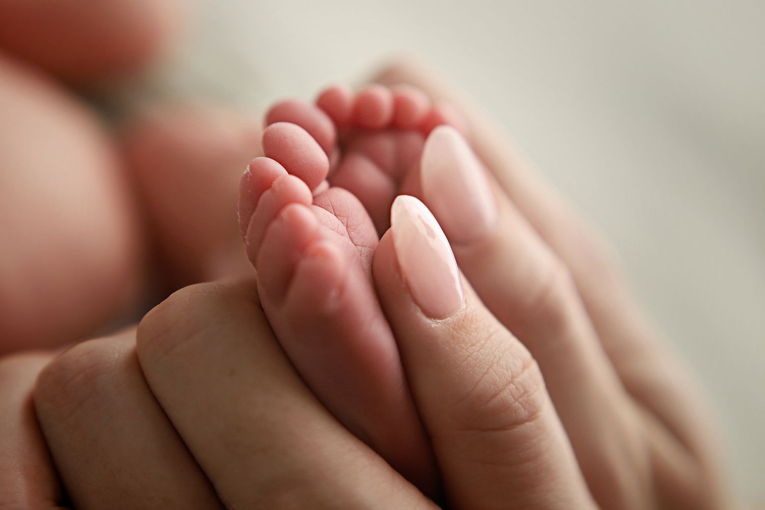 Close-up of a mother's hands gently cradling tiny newborn baby feet, showcasing the delicate bond between parent and child. Newborn photos