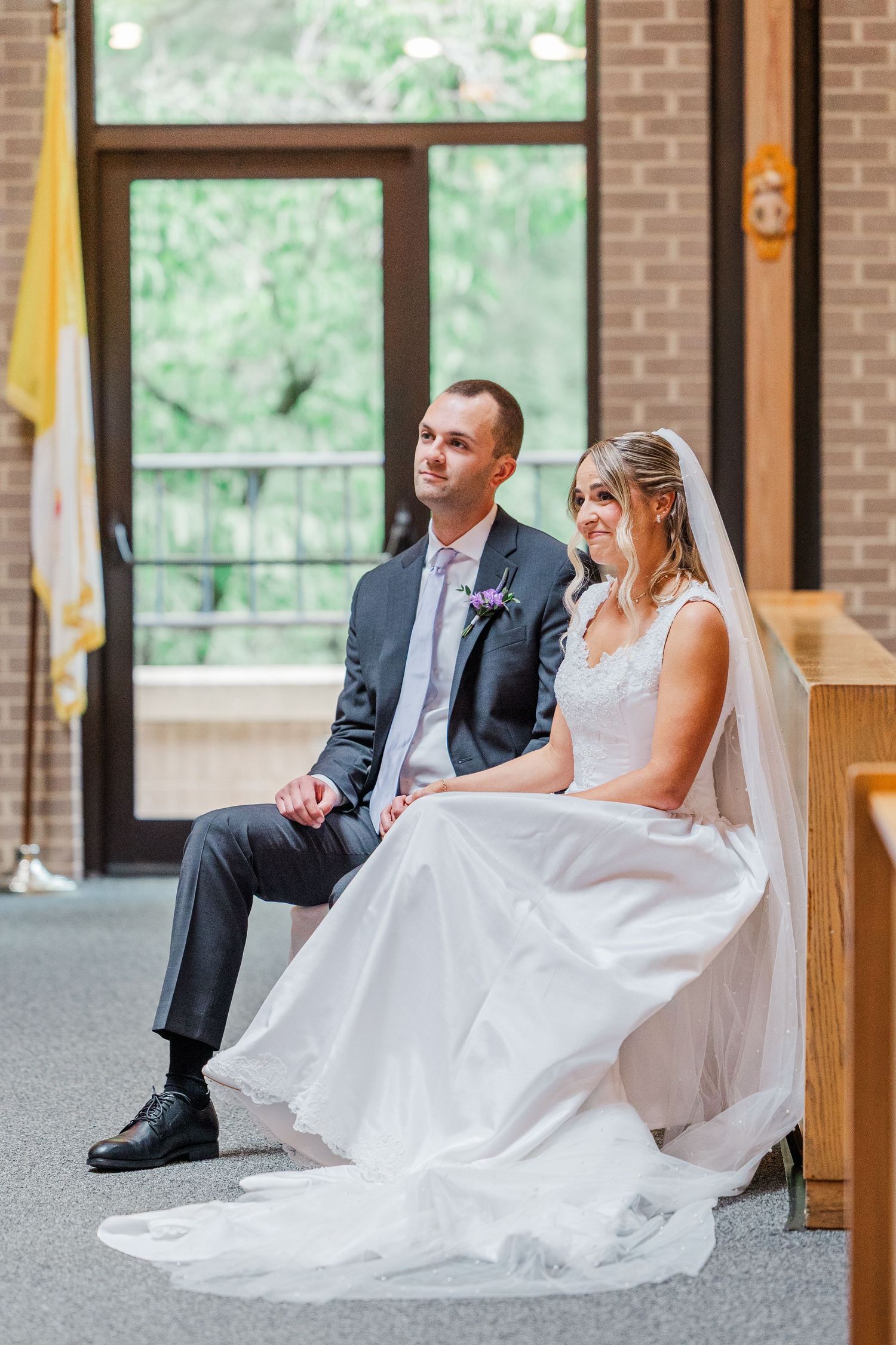 Bride and groom sitting together in a church during their wedding ceremony, bride in white gown with veil.