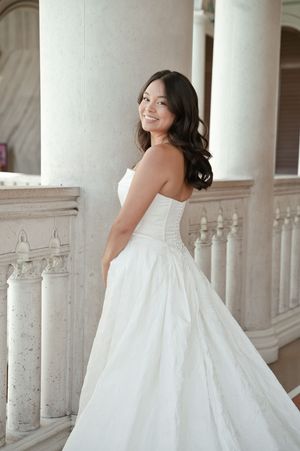 Smiling bride in strapless white ball gown poses gracefully near elegant marble columns in a grand venue.