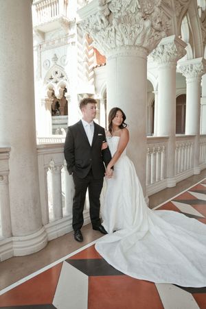 Bride and groom pose elegantly on an ornate marble balcony with white columns at The Venetian Las Vegas.