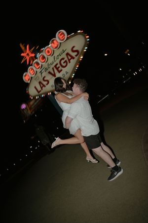 Couple embracing and jumping in front of the iconic Welcome to Fabulous Las Vegas sign at night.