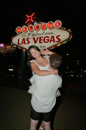 Joyful couple embraces in front of the iconic Welcome to Fabulous Las Vegas sign at night.
