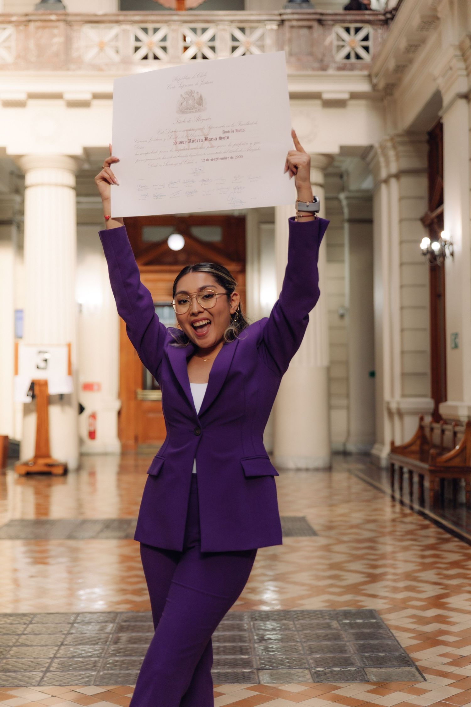 Excited woman in purple suit raising official certificate overhead in celebration.