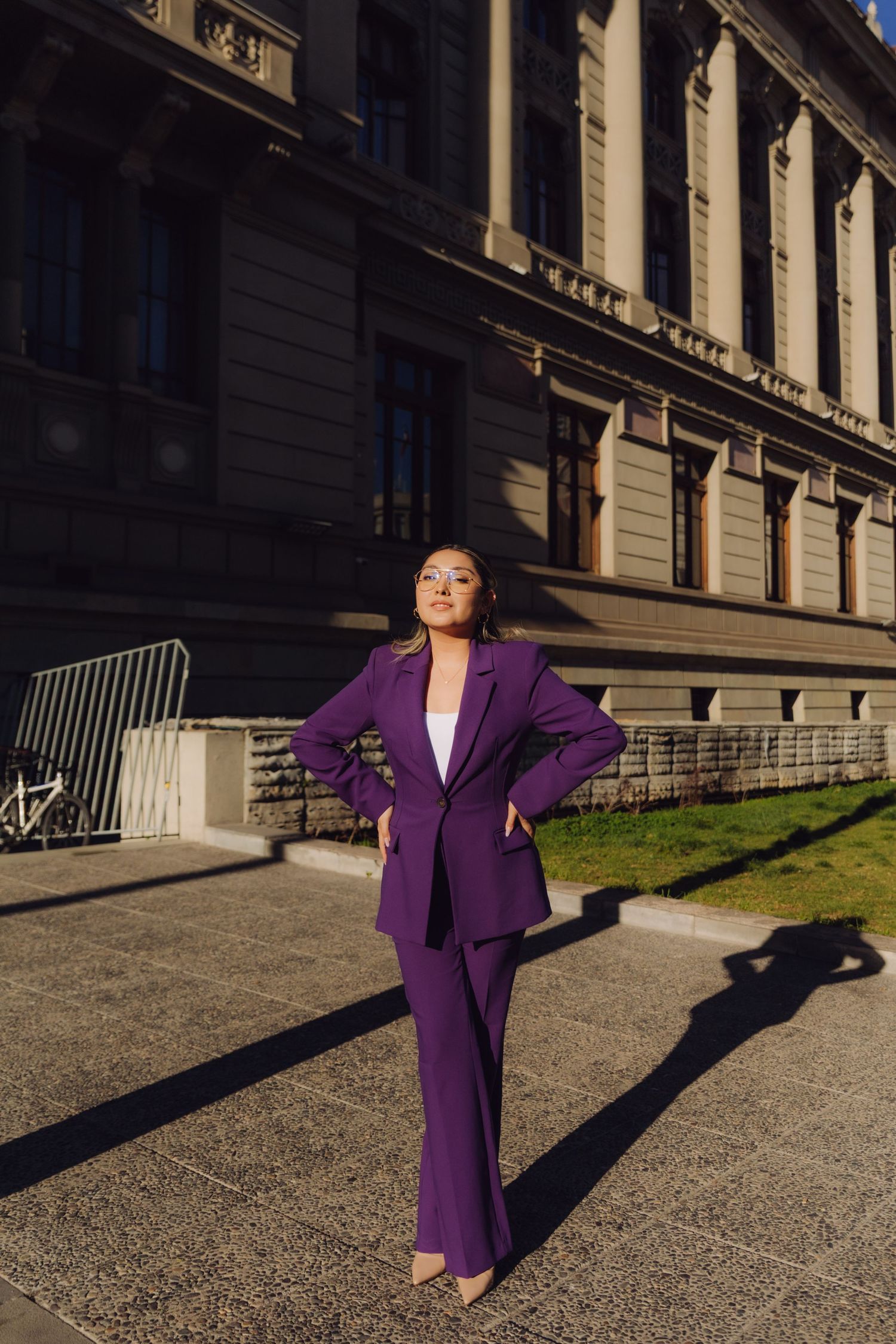 Confident woman in purple pantsuit poses outside grand neoclassical government building.
