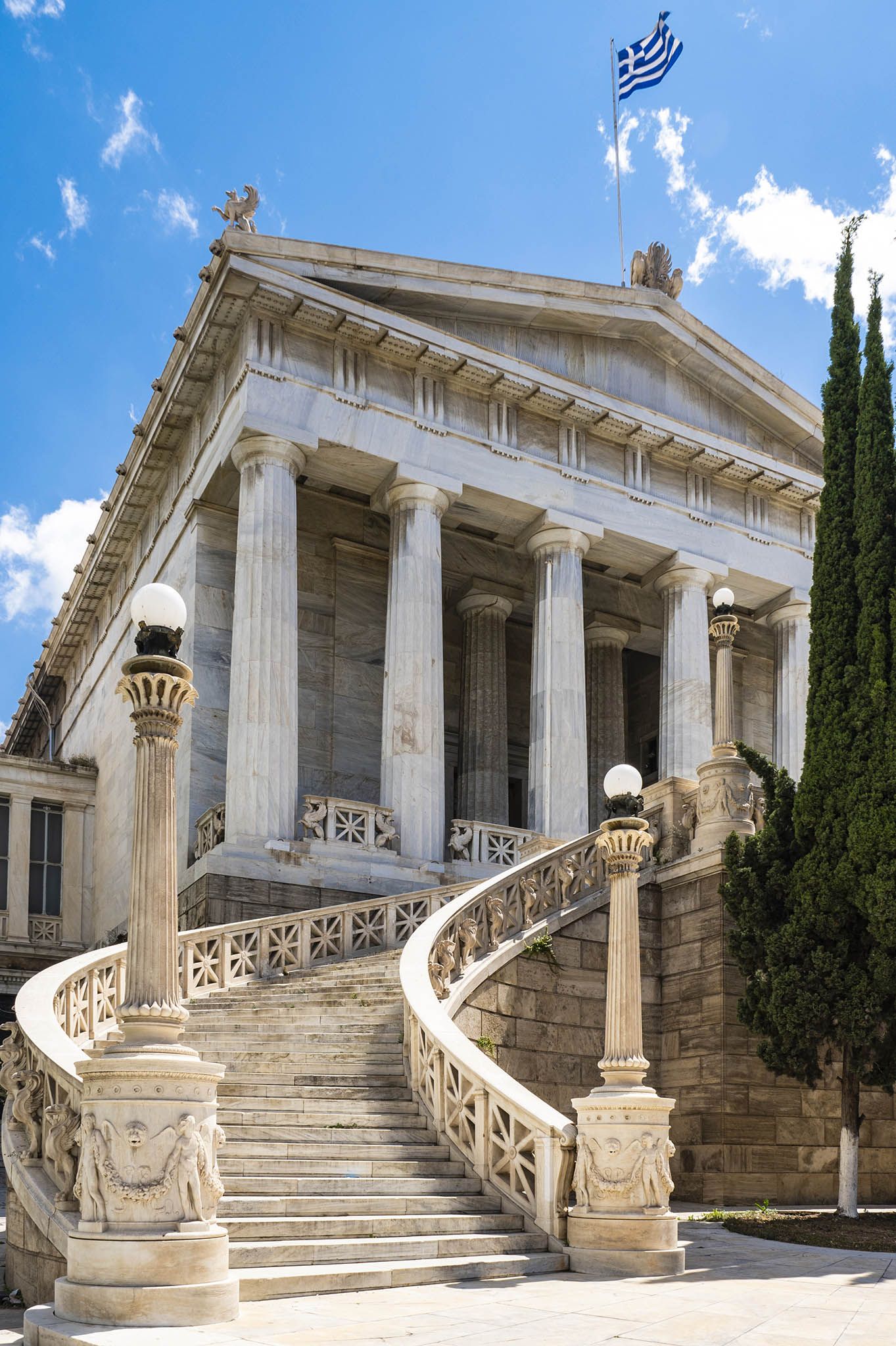 Classical Greek-style building with grand columns and sweeping stone staircase under blue sky.