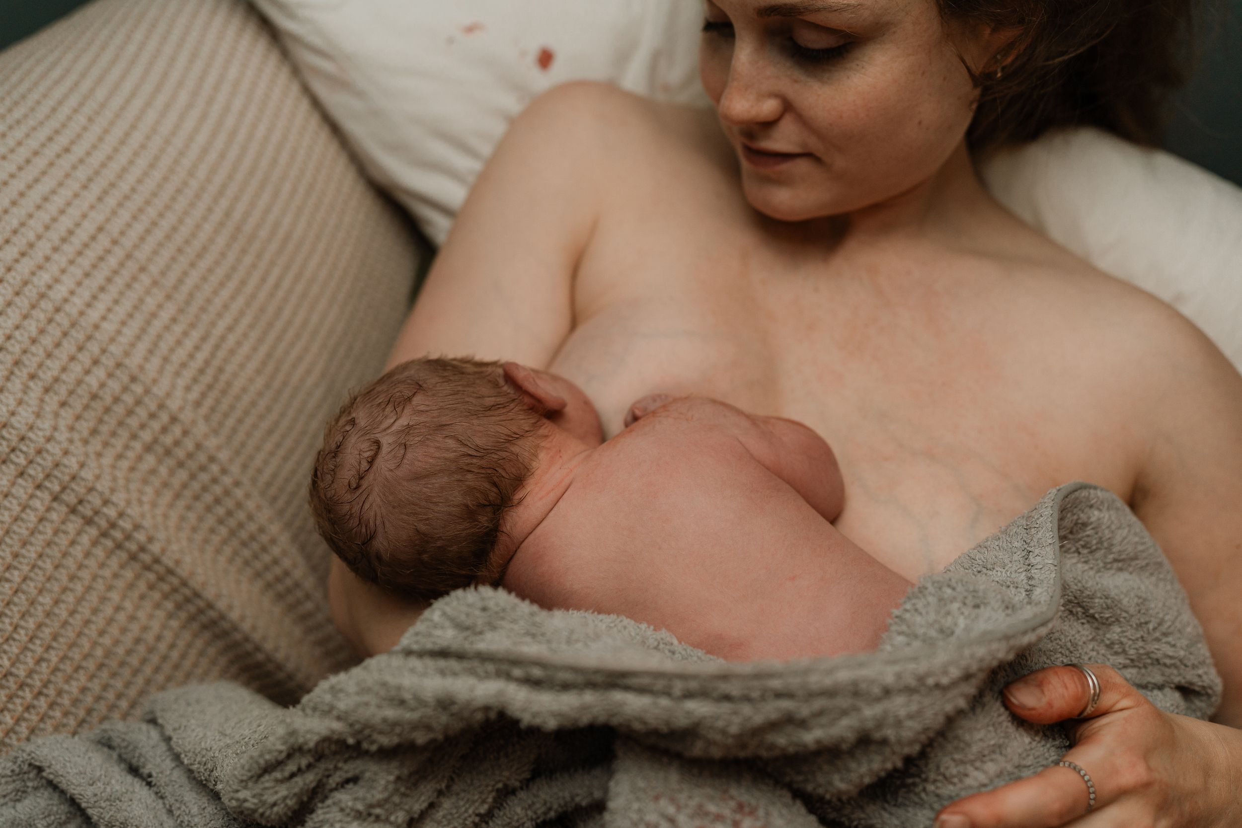 Mother holding newborn baby skin-to-skin after home birth in Lancashire, wrapped in gray blanket during golden hour.