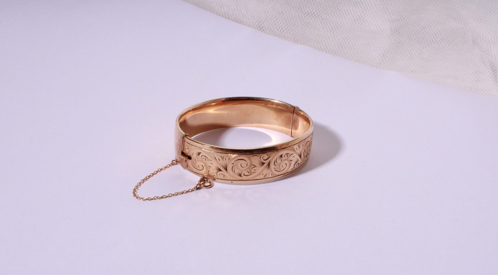 Vintage gold bangle bracelet with floral engraving and safety chain.