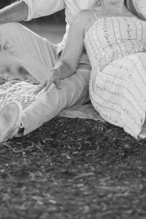 Black and white photo of a couple sitting together on the ground, the woman in a lace dress holding the mans hand.