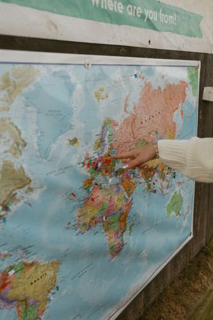 A hand pointing to Europe on a colorful world map with pins, under a sign reading where are you from.