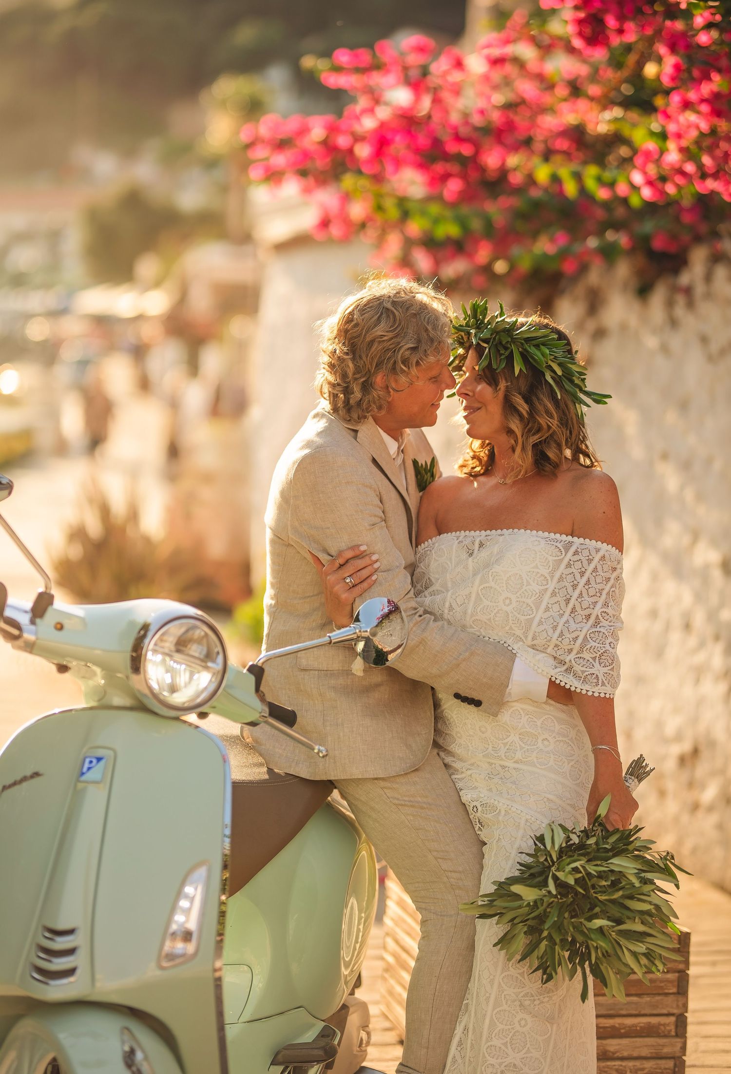 Bride and groom share a romantic moment beside a mint green Vespa scooter, surrounded by pink bougainvillea in warm sunlight.