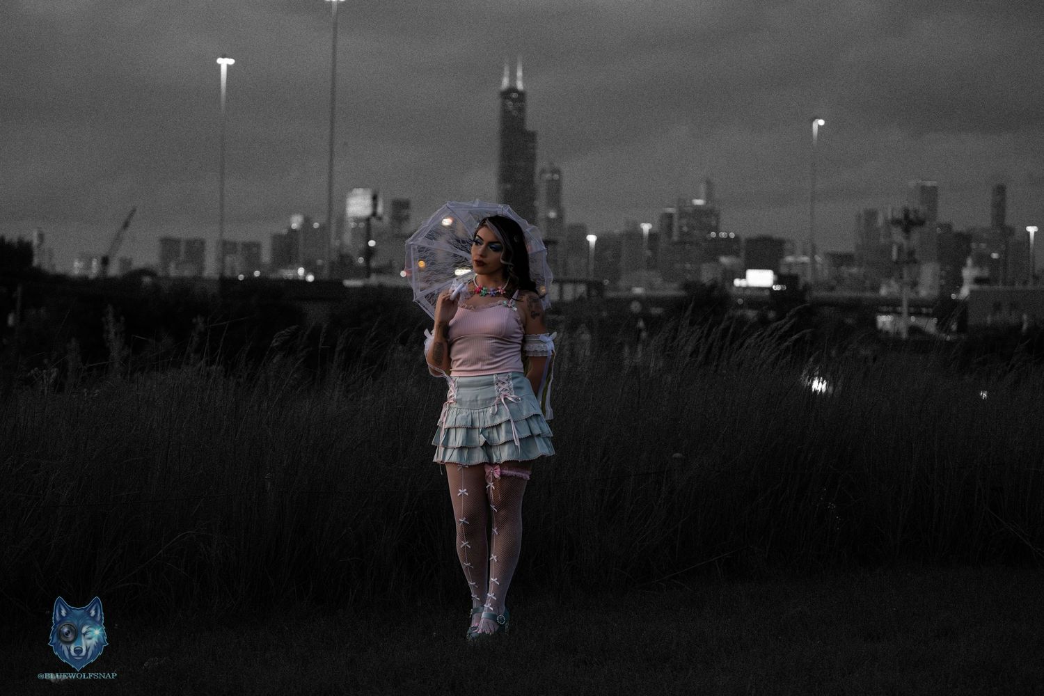 Girl in pink top and blue skirt holds sparkler in front of Chicago skyline at dusk in selective color photo.