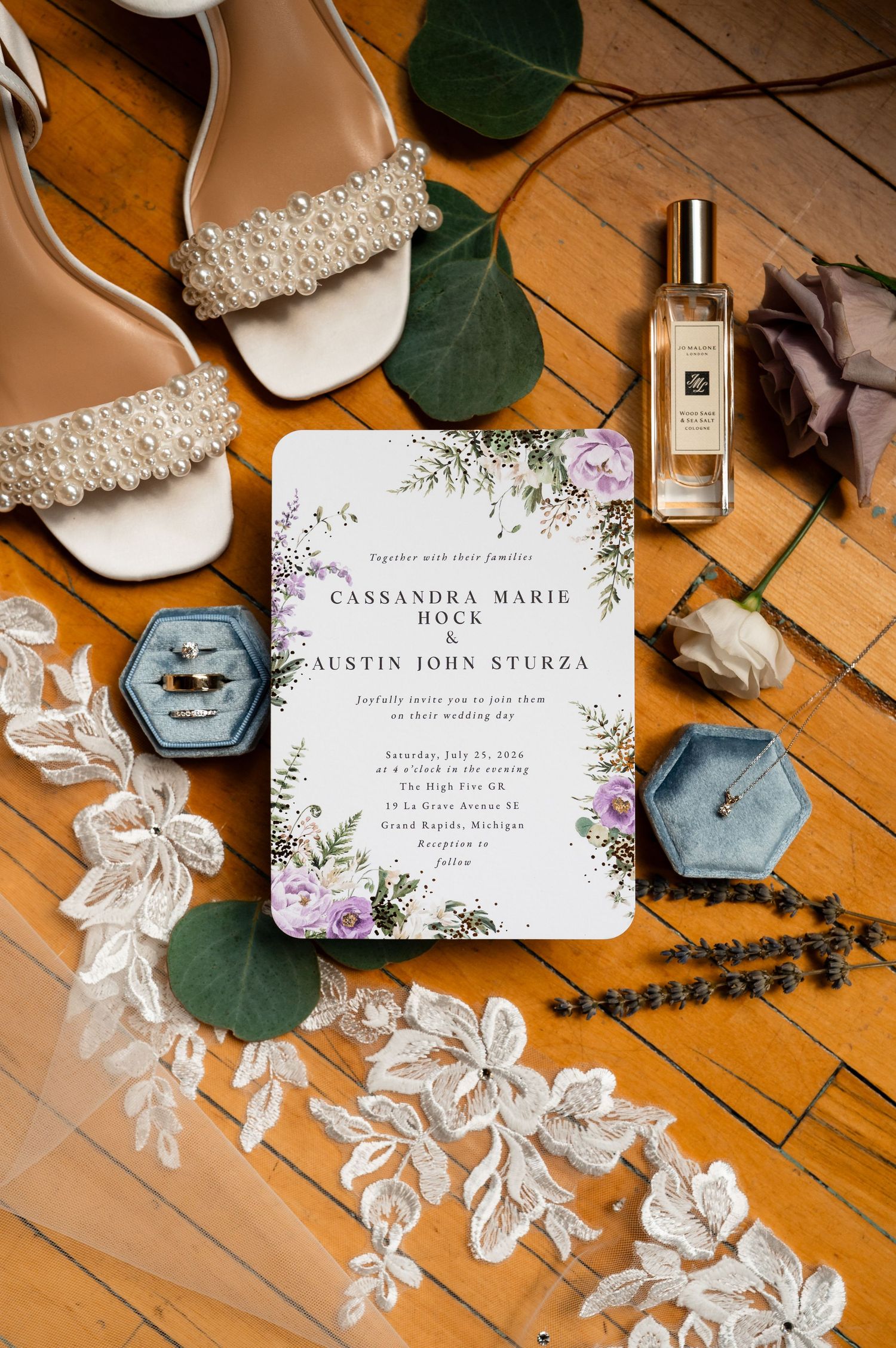 Wedding flat lay featuring invitation for Cassandra Hock and Austin Sturza, pearl heels, rings, lace, and Jo Malone perfume.