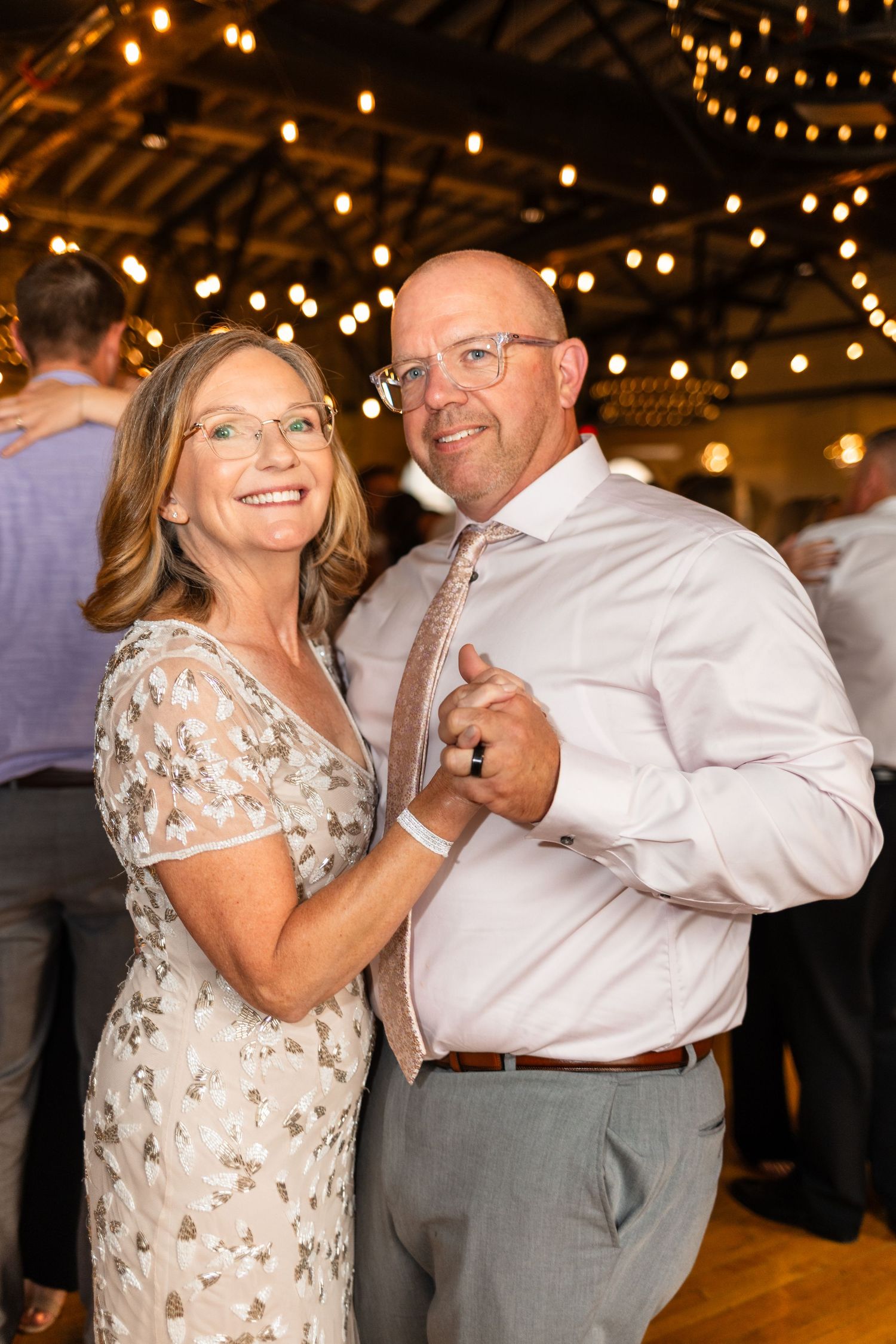 Couple dancing and smiling at a wedding reception with warm string lights overhead.