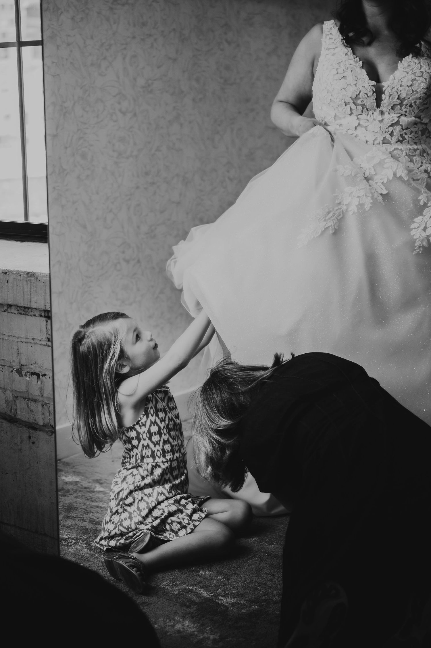 Black and white photo of two young children helping a bride with her wedding dress while seated on the floor.