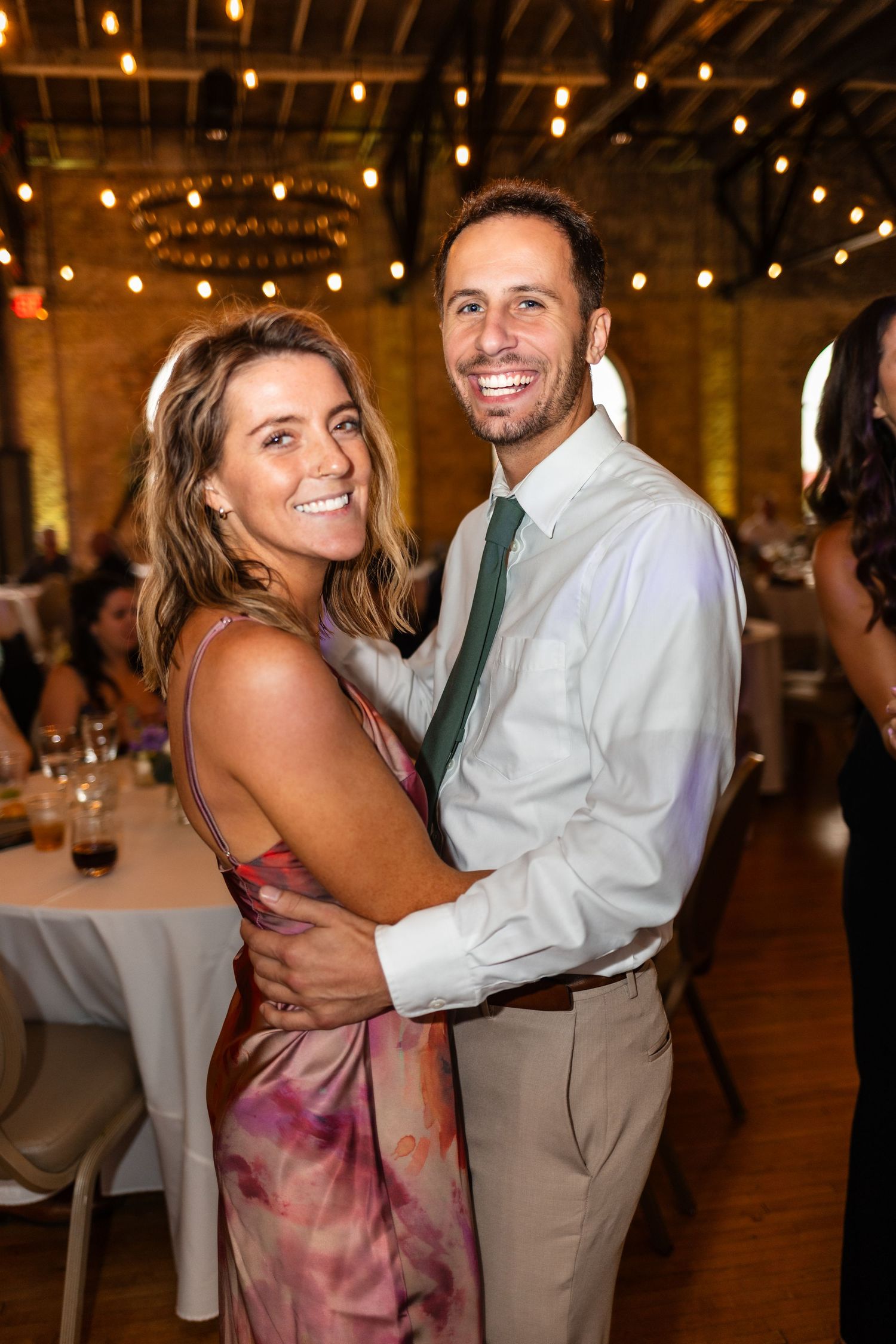 Smiling couple embracing and dancing together at an elegant wedding reception with string lights.