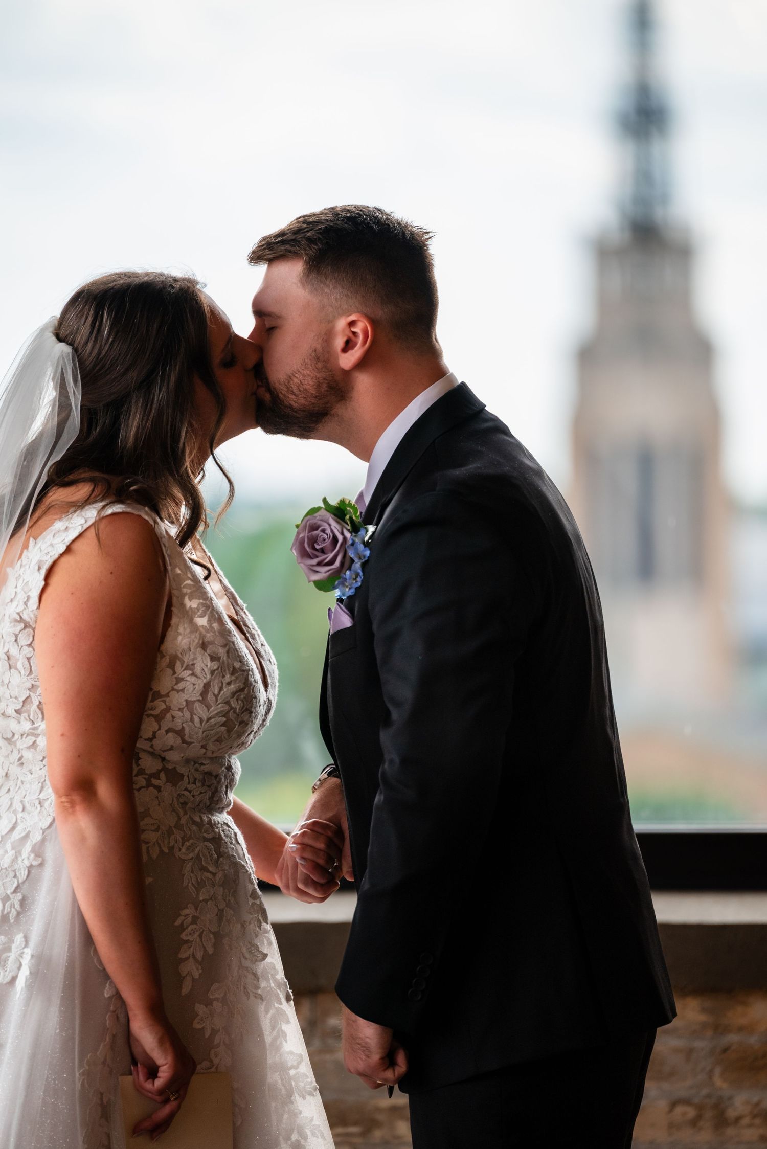 Bride and groom share a romantic kiss, with a church tower visible in the background.