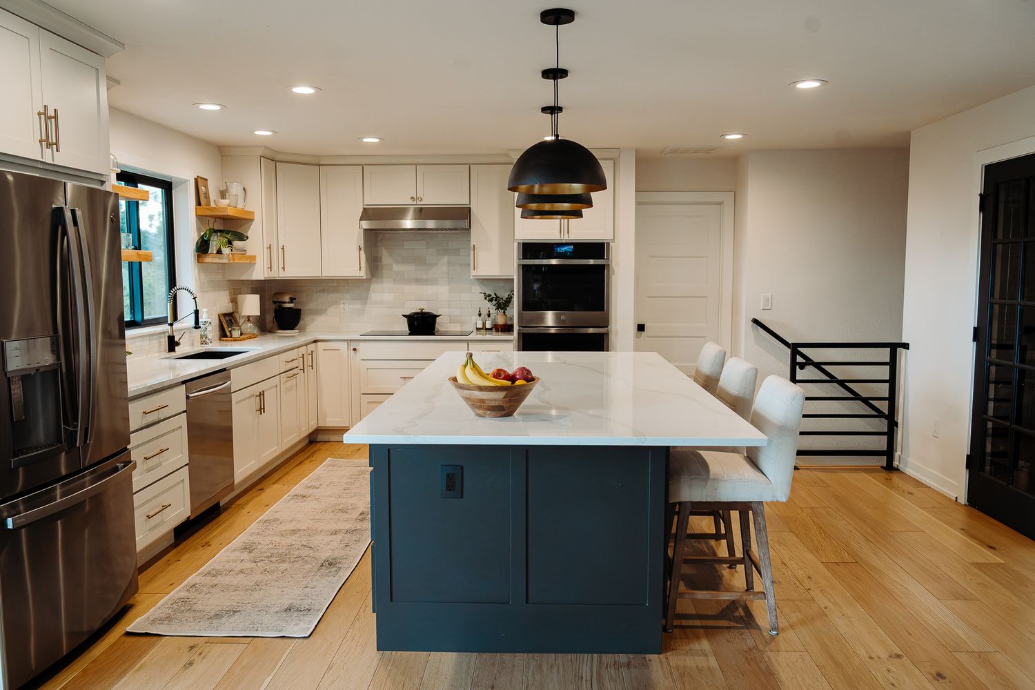 Modern kitchen with navy blue island, white cabinets, stainless steel appliances, quartz countertops, and hardwood floors.