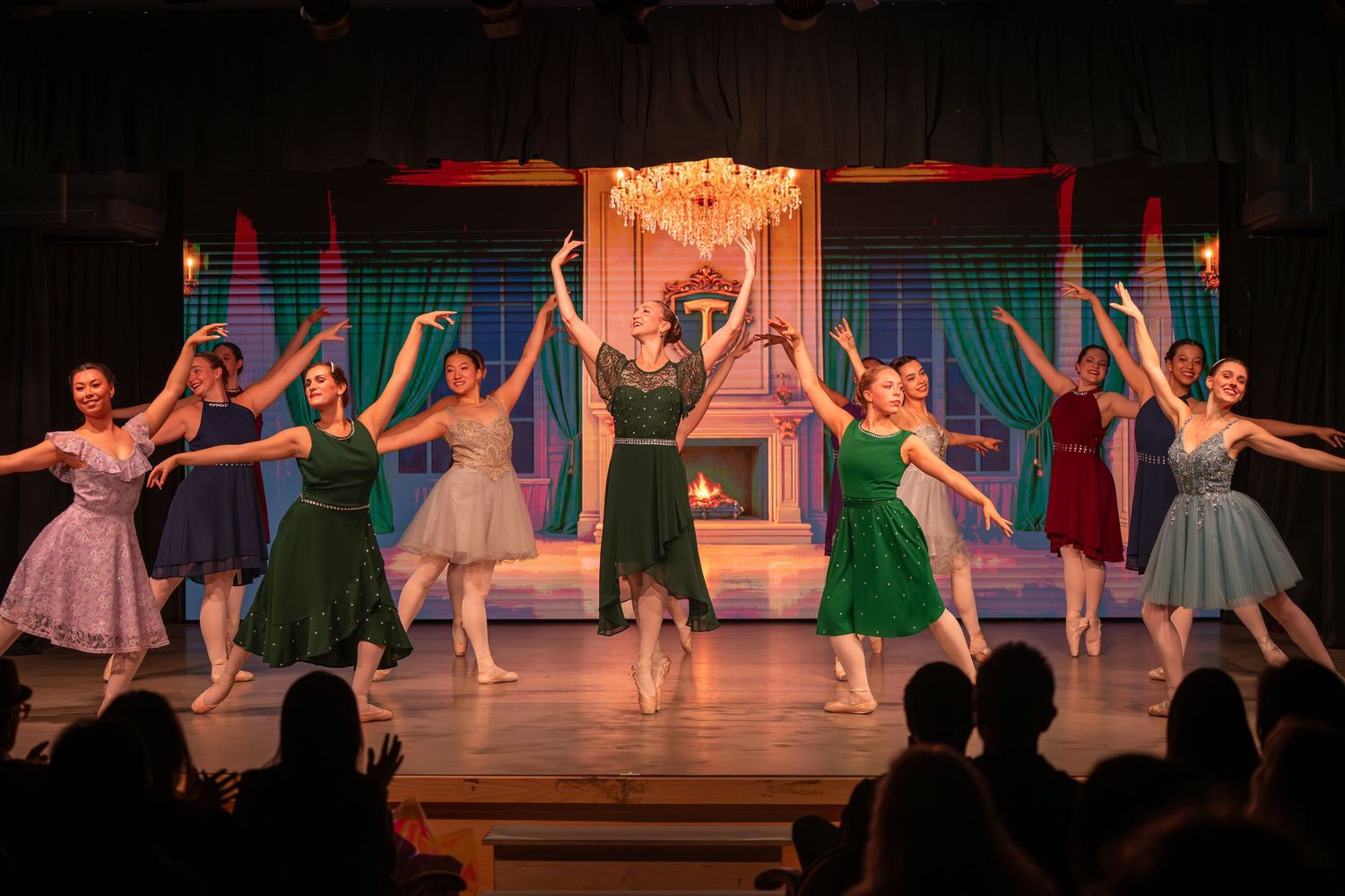 Ballet dancers in colorful dresses perform on stage with elegant backdrop during a graceful ensemble dance recital.