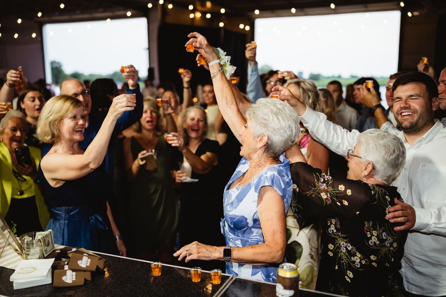 Guests raising glasses in a celebratory toast at an indoor event with string lights in the background.