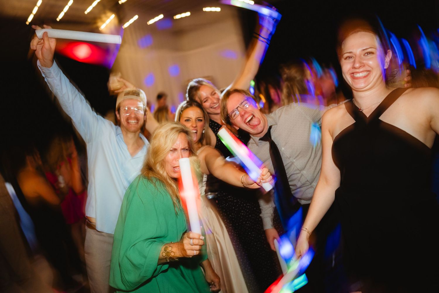 Group of joyful party guests dancing and holding glowing light sticks at a festive celebration event.