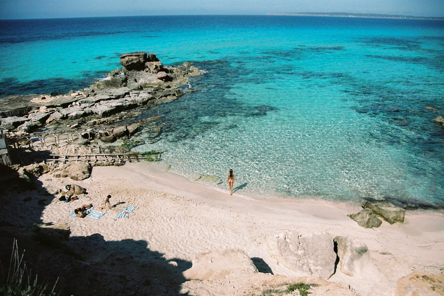 Serene tropical beach with white sand, calm turquoise waters, and lush green mountains under a partly cloudy sky.