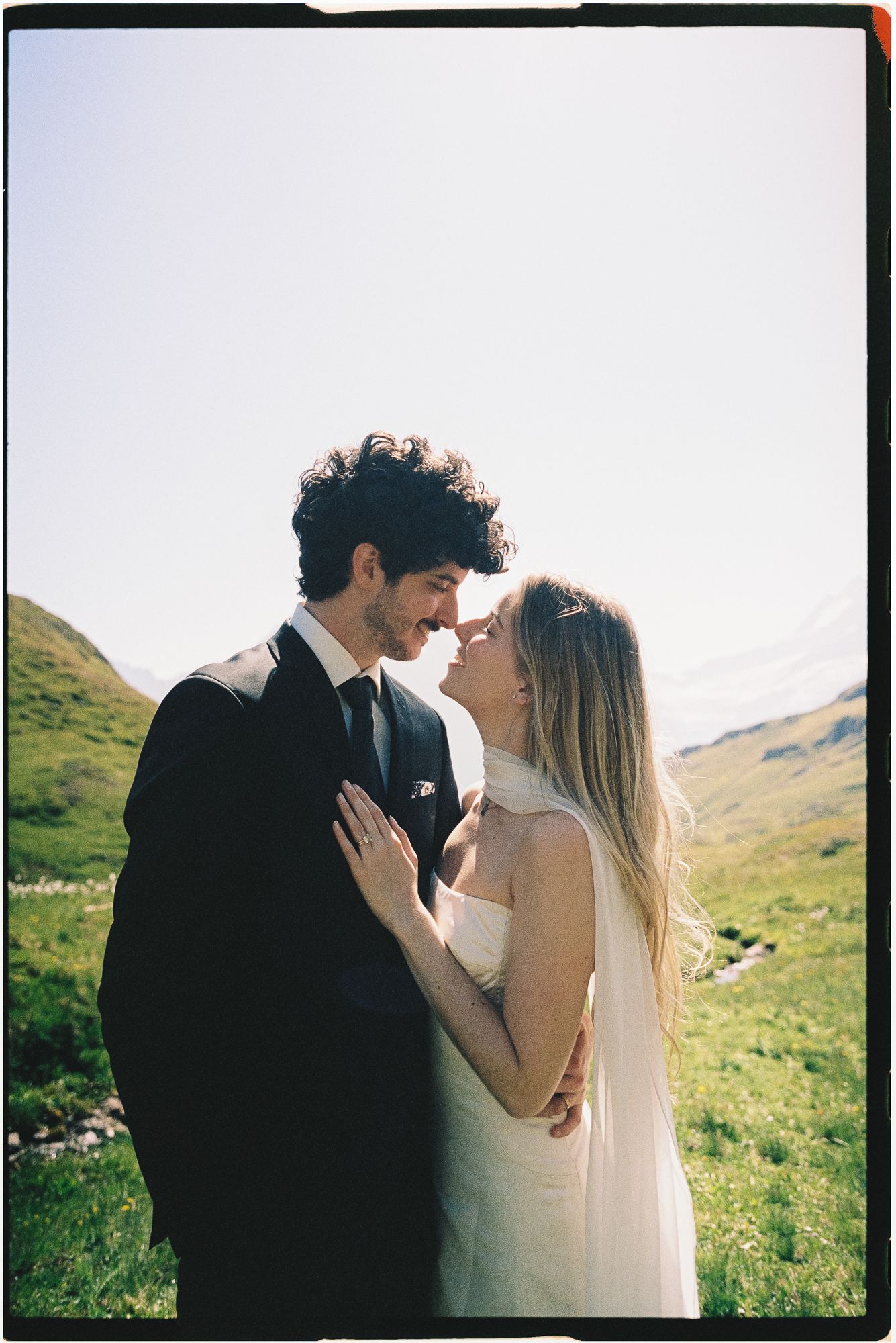 Black and white photo of a smiling couple lying on grass, gazing at each other in a romantic outdoor setting.