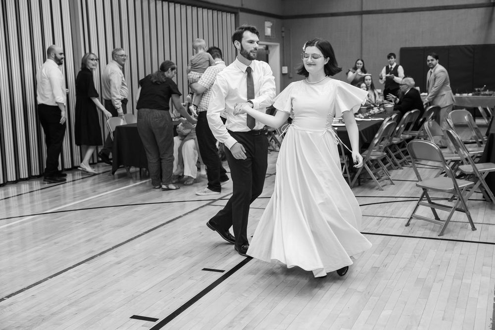 Black and white photo of a bride and groom dancing joyfully at their wedding reception in a decorated hall.
