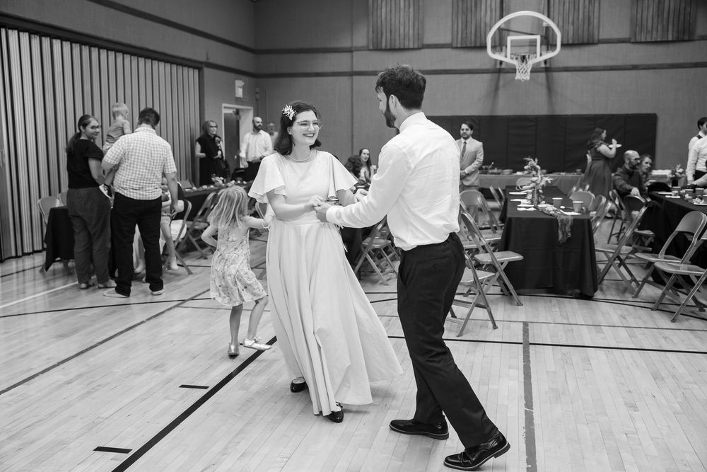 Bride and groom share first dance in gymnasium wedding venue, black and white photo.