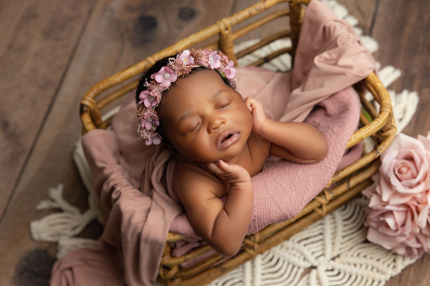 Sleeping newborn baby wrapped in teal swaddle inside a small bucket with a green pillow.