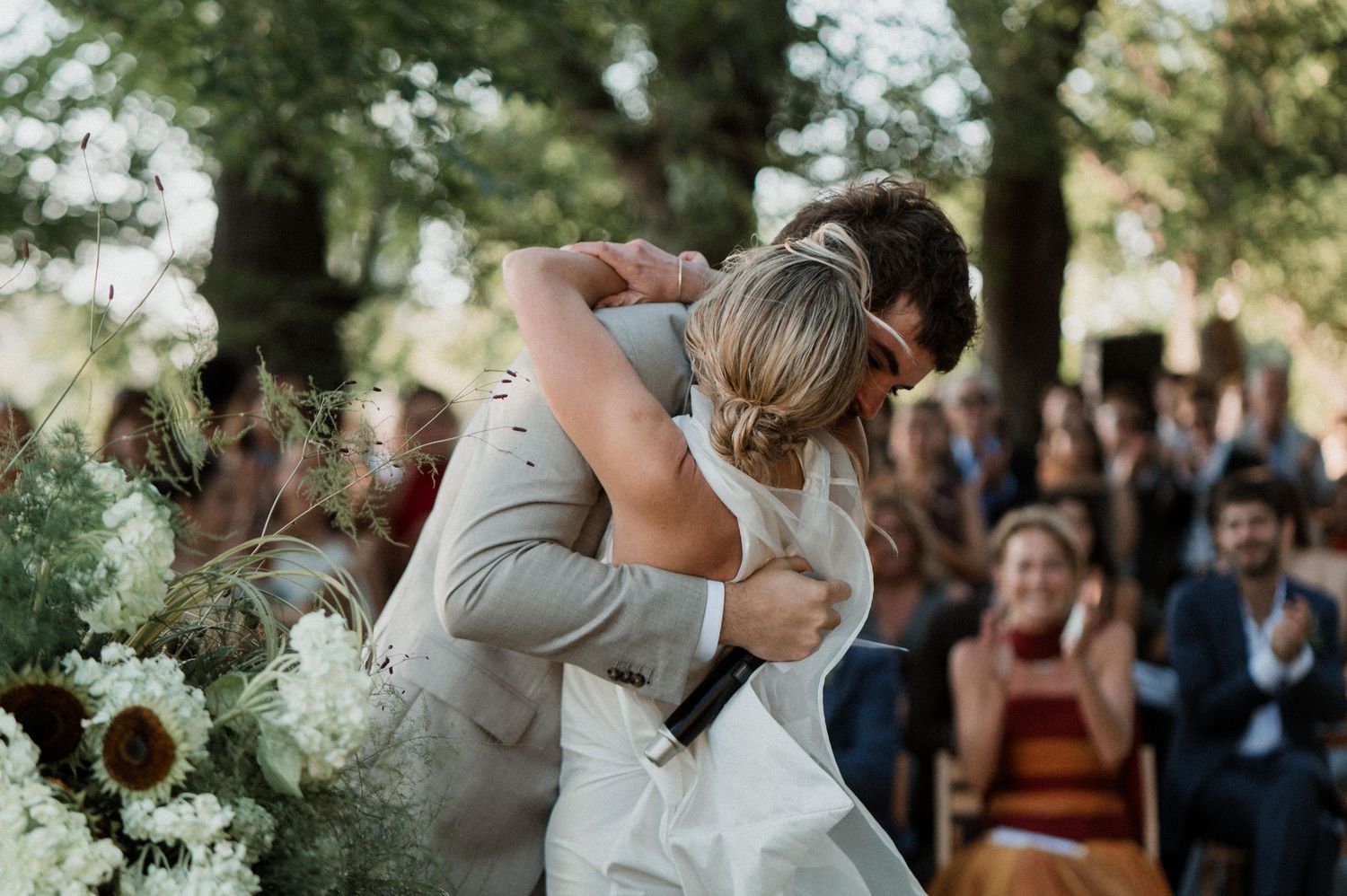 A bride in a white dress and groom in gray run through a lush green meadow field together.