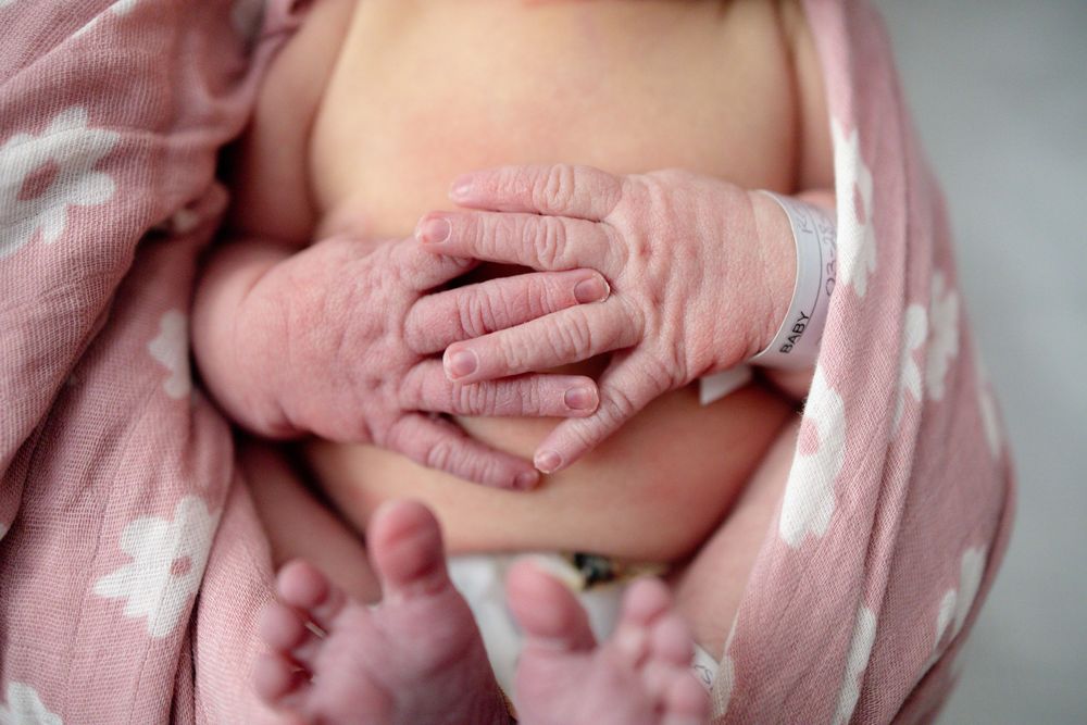 Close-up of a newborn baby's tiny hands and feet wrapped in a soft pink floral swaddle blanket at Parkwest Medical Center in Knoxville, TN.
