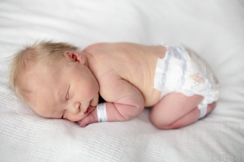 Peaceful newborn baby sleeping curled up on white blanket wearing a diaper at Parkwest Medical Center in Knoxville, TN.