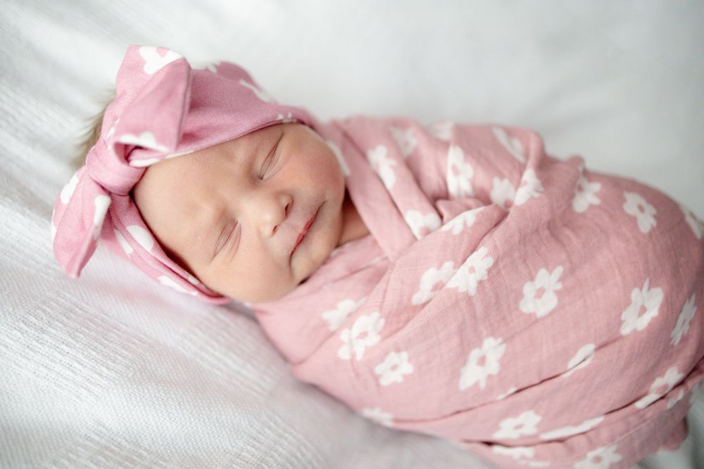 Newborn baby girl sleeping peacefully swaddled in pink floral muslin wrap with matching bow at Parkwest Medical Center in Knoxville, TN.