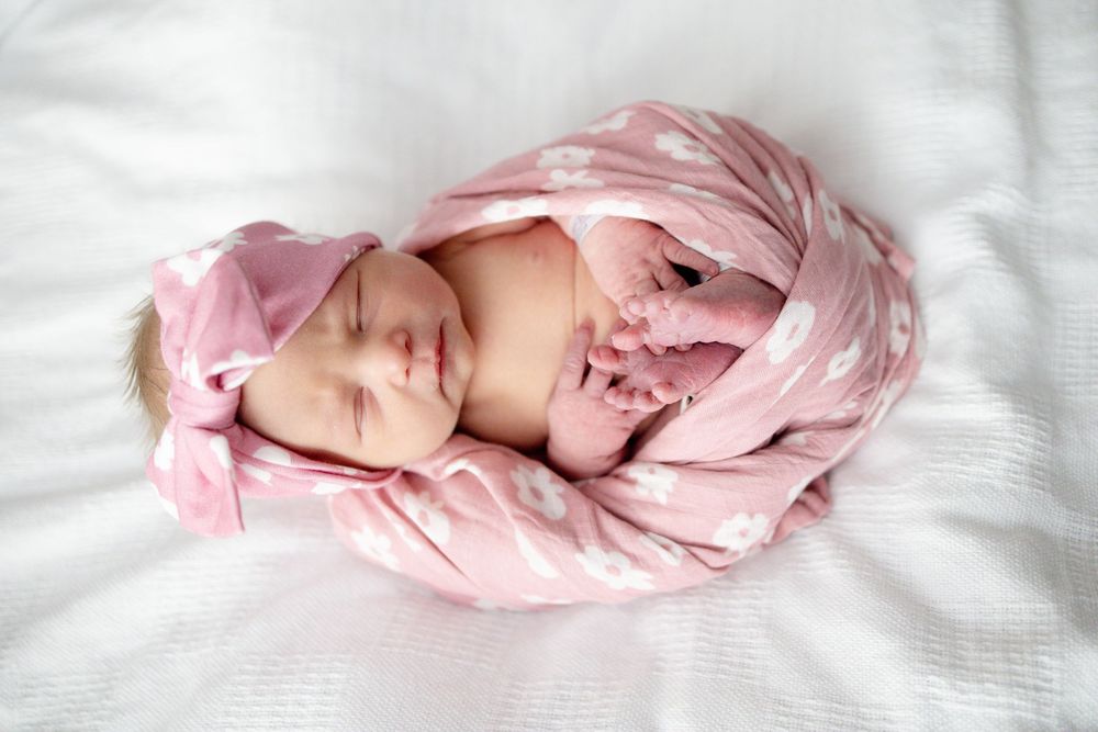 Baby girl sleeping peacefully wrapped in soft pink floral swaddle blanket on a white background at Parkwest Medical Center in Knoxville, TN.