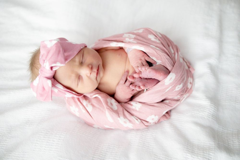 Newborn baby girl sleeping peacefully wrapped in a pink polka dot swaddle blanket with matching bow headband at Parkwest Medical Center.