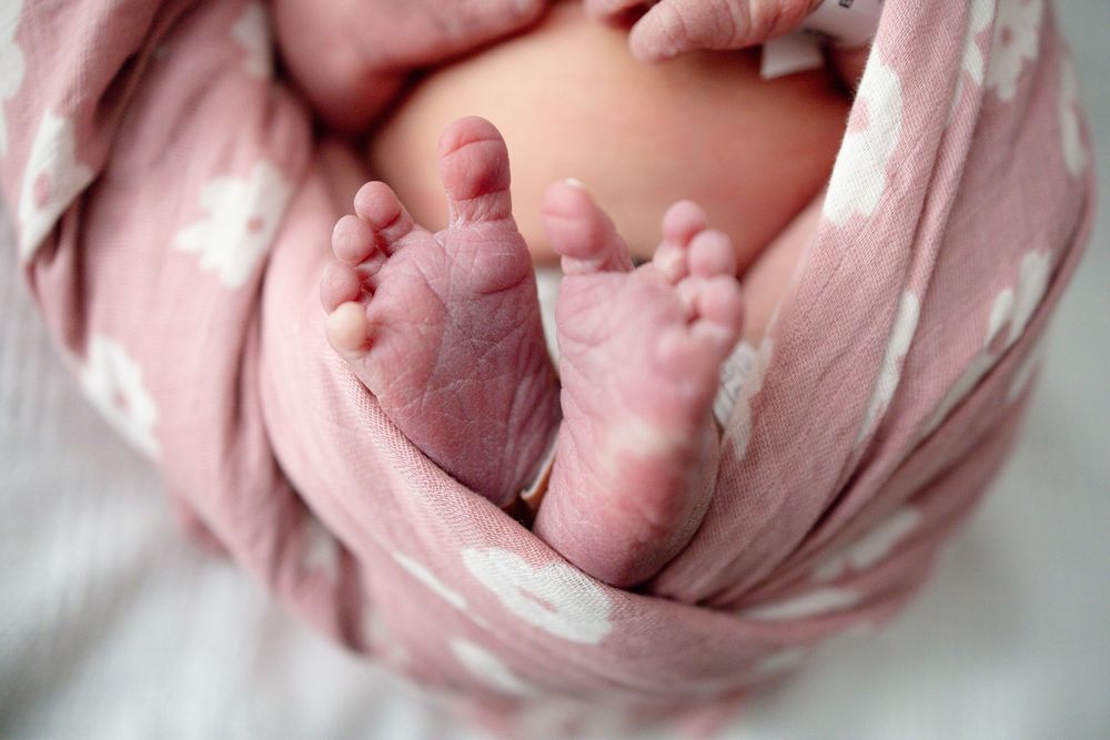 Close-up of newborn baby feet wrapped in a soft pink muslin swaddle blanket with white pattern at Parkwest Medical Center in Knoxville, TN.