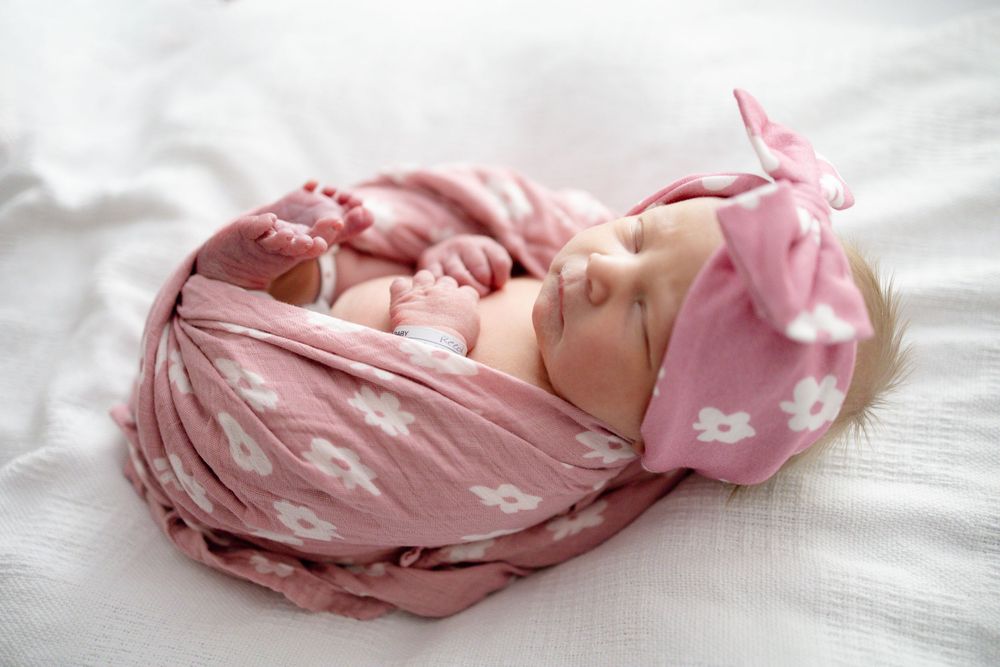 Newborn baby sleeping peacefully wrapped in a pink floral swaddle blanket with matching bow headband at Parkwest Medical Center in Knoxville