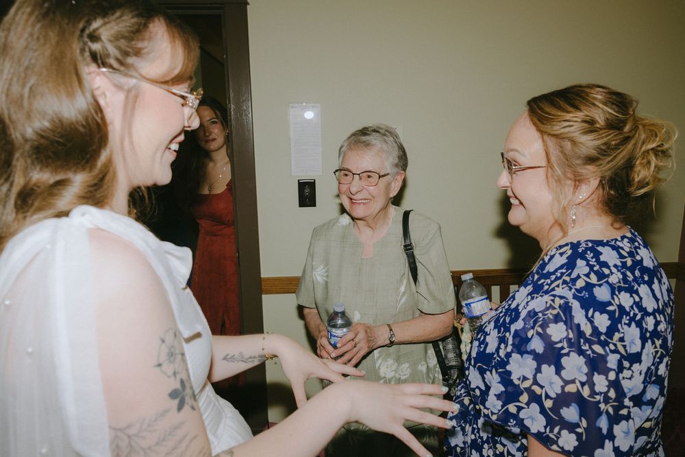 Three women laughing and socializing at an indoor gathering, sharing a joyful conversation together.