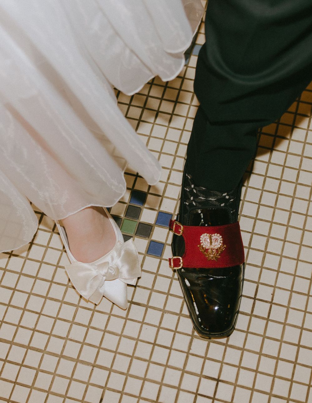 Close-up of wedding couple's shoes on tiled floor, bride in white satin heels, groom in black patent Gucci loafers.