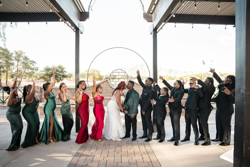 Wedding party celebrating under a pavilion, bridesmaids in green and red gowns with groomsmen in black suits.