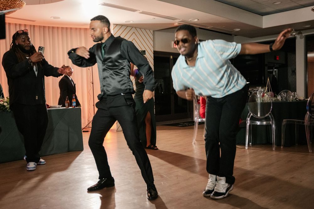 Three men dancing energetically at an indoor event on a wooden dance floor in a banquet hall.